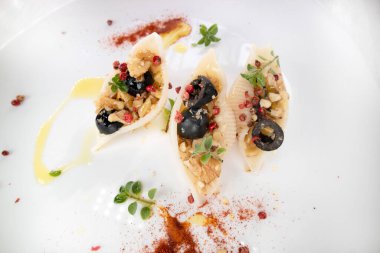 Mediterranean diet presentation of a plate of pasta shells topped with black olives and walnuts in olive oil 