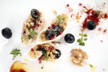 Mediterranean diet presentation of a plate of pasta shells topped with black olives and walnuts in olive oil 