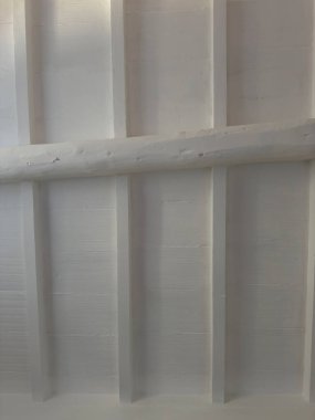 Detail of a ceiling with wooden planks and exposed beams, all painted white, creating a clean and bright atmosphere. 