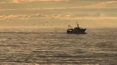 Çekim, tipik bir İtalyan balıkçı teknesinin arka plandaki dağlara ve dramatik gökyüzüne karşı yavaşça limana geri dönüşünü takip ediyor.. 
