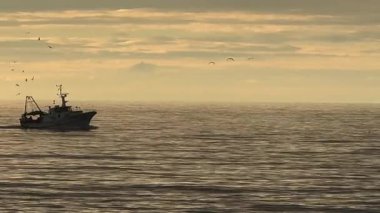 Çekim, tipik bir İtalyan balıkçı teknesinin arka plandaki dağlara ve dramatik gökyüzüne karşı yavaşça limana geri dönüşünü takip ediyor.. 