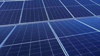 Yenilenebilir ve sürdürülebilir enerjiyi temsil eden mavi fotovoltaik hücrelere odaklanan modern bir güneş çiftliği dizisinin yüksek kaliteli drone görüntüsü.