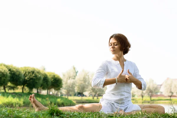 Girl in white clothes practicing yoga at the river-bank — Stock Photo, Image