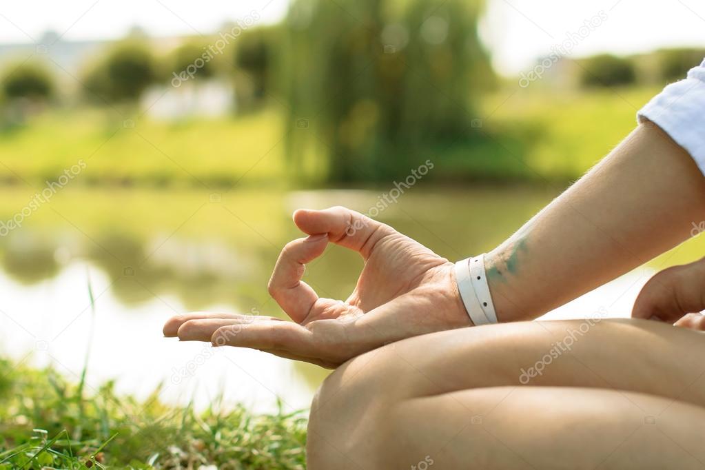 Closeup of the female hand put in gyan mudra. Woman sits on the grass at the river