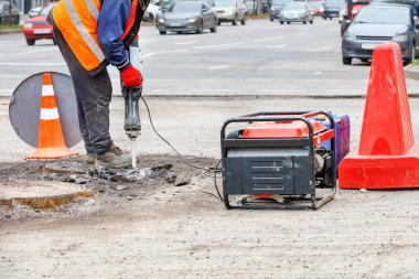 Bir işçi yolun bir bölümünü elektrikli matkapla tamir ediyor. Arka planda da da geçen bulanık arabalar var..