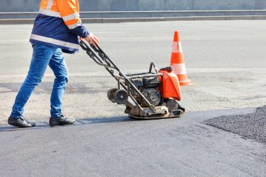 Bir yol işçisi, otoyolda asfaltı bir petrol titreşim sıkıştırıcı ile sıkıştırır..
