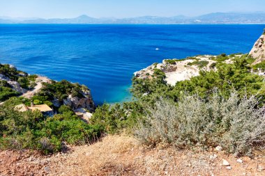 Yunan Körfezi 'nin kayalık yamaçlarında koyu bir çalı yetişir. Sahildeki mavi bir lagünün arka planına karşı, çok güzel bir manzarası vardır. Boşluğu kopyala.