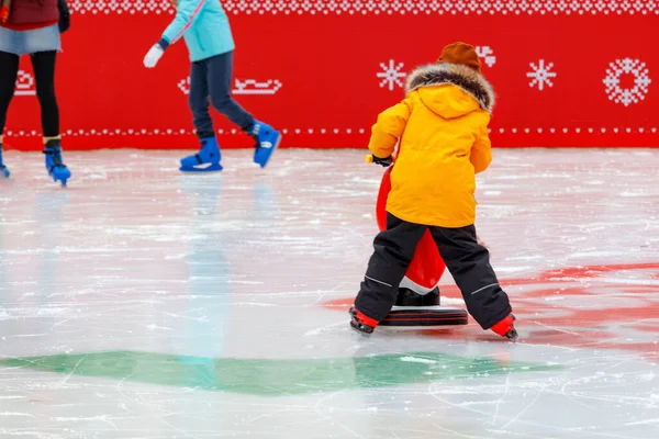 小男孩学会了站在室外滑行 紧紧地抓住助手 这是一只玩具企鹅 背景是在模糊的滚动的孩子们 复制空间 选择性焦点 — 图库照片