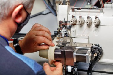 Eski bir ustanın elleri modern bir elektrikli dikiş makinesi kurdu ve dikişlerin kalitesini kontrol etti..