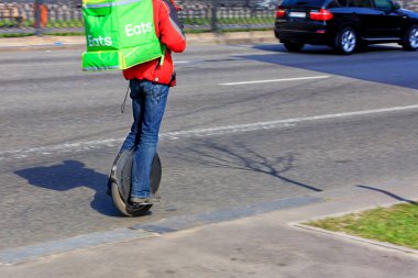 Yemek dağıtım servisinden genç bir adam sırtında yeşil bir sırt çantasıyla tek tekerlekli bisiklete biniyor ve yemek dağıtıyor..