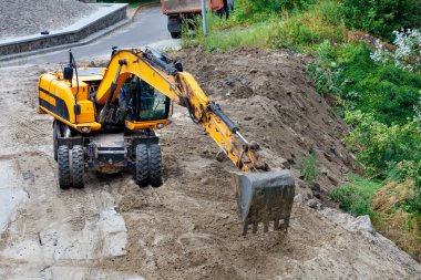 On a cloudy summer day, a construction excavator clears a construction site for the foundation of a future home.