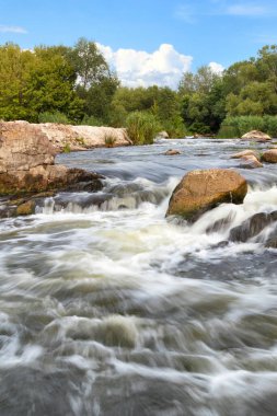Güney Böceği 'nin fırtınalı su akıntıları, kayalık akıntıları aşar, yeşil bitki örtüsü boyunca koşar hafif bulutlu mavi yaz gökyüzünün arka planına karşı. Dikey resim, boşluğu kopyala.