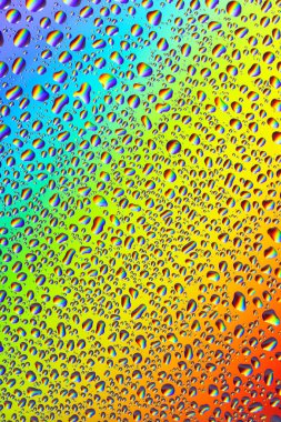 Su parlak bir gökkuşağı arka planına düşer ve gökkuşağının yansıması, yakın plan, yüksek çözünürlük, dikey görüntü.