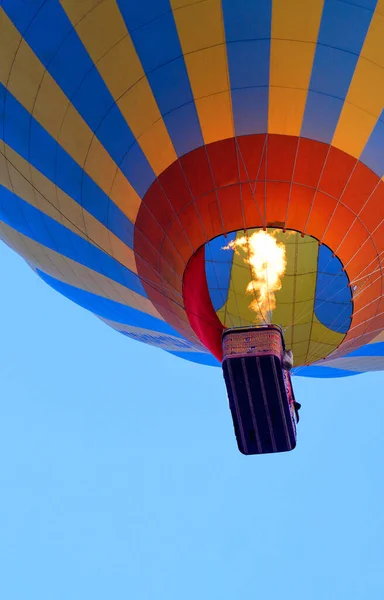 Flying in a hot air balloon, the flame of the burner fire heats the air, raising the balloon with a basket high into the sky, close-up, bottom view. Copy space, vertical image.
