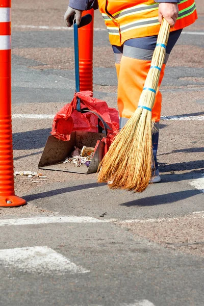 A cleaning lady in a bright orange uniform collects trash from the sidewalk on a sunny day. Vertical image, copy space.