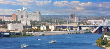 Kyiv 'in panoramik manzarası, ön planda Dnipro Nehri, su yüzeyinde yüzen kayıklar, setin arka planında, ufukta ormanlar, şehir binaları ve güzel bir gökyüzü..