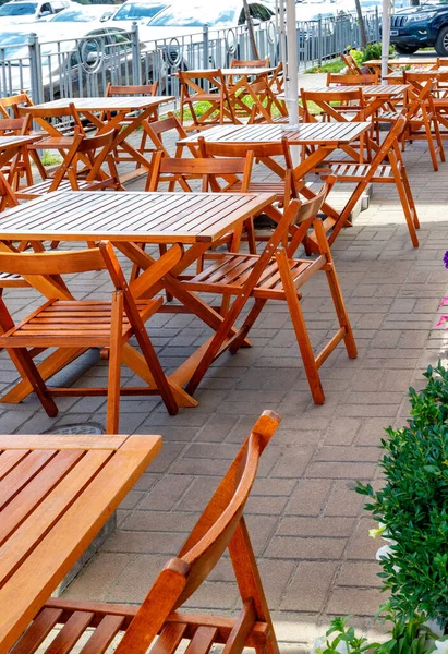 Boş ahşap masaları olan boş bir sokak kafesi geçen arabalı bir şehir sokağının arka planında. Dikey resim, boşluğu kopyala.