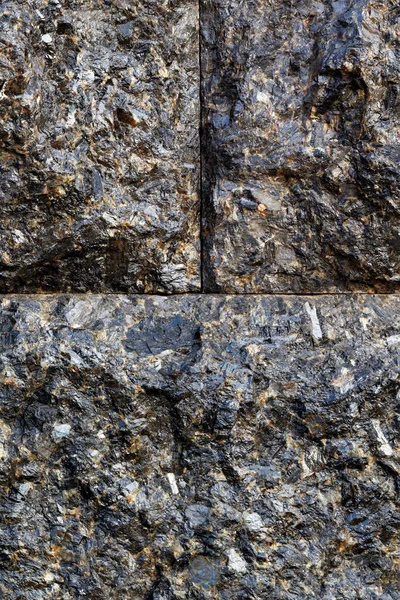 Beautiful texture of black granite blocks tightly adjacent to each other with a conditional division of the image into parts. Vertical image, copy space.