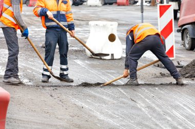 Parlak turuncu yansıtıcı yelekli trafik çalışanları, yol bölümlerinin tamir edilen eklemlerindeki enkazı temizliyor. Boşluğu kopyala.