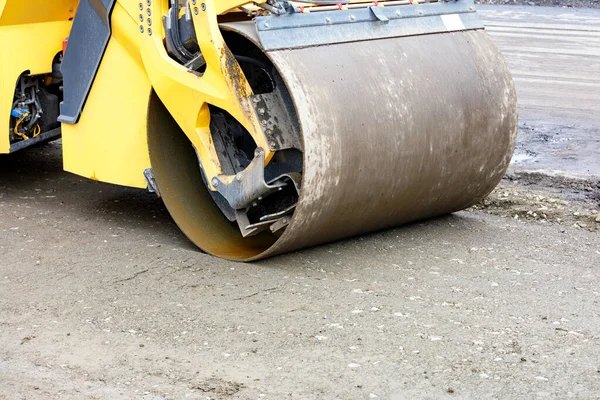 The metal cylinder of the yellow road vibratory roller powerfully ramps the sandy base at the construction site. Copy space, close-up.