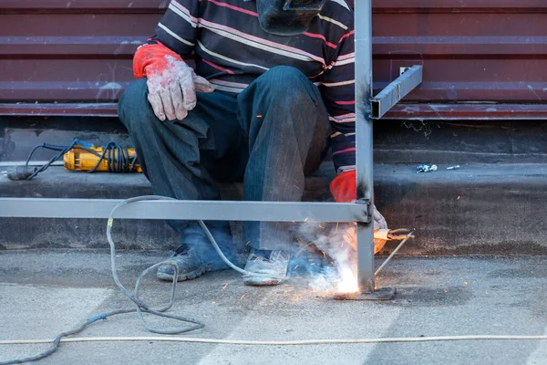 A bright flash of electric arc as a seated welder installs and reinforces a metal fence around the house. Copy space.