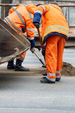 Yol işçilerinden oluşan parlak turuncu yansıtıcı üniformalı bir ekip yolun bir kısmını temizliyor. Uzayı kopyala Dikey resim.