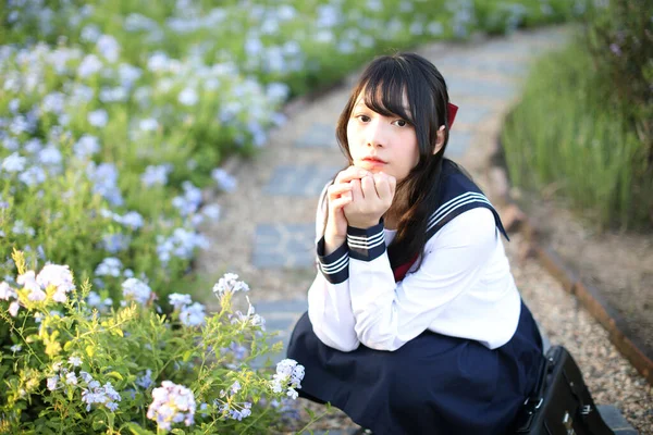Asian school girl sitting with flower garden background
