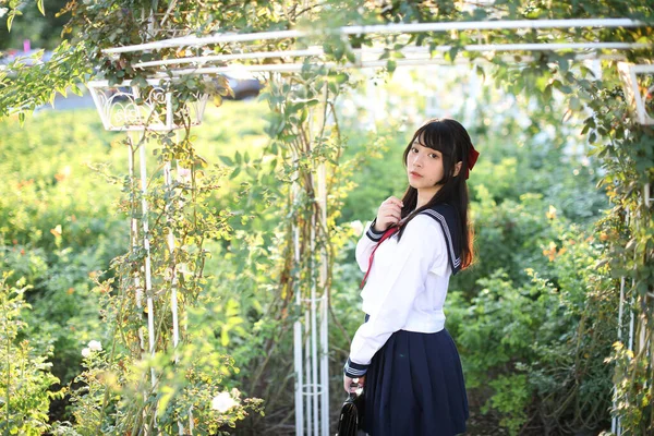 アジアの女子高生歩くと花の庭の背景を見ます — ストック写真