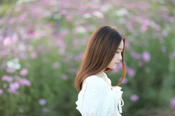 在粉色宇宙花朵背景上穿着白色衣服的年轻貌美的女人 — 图库照片