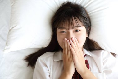 Japon okul üniformalı kız portresi uyur ve beyaz renkli yatak odasındaki kameraya bakar.