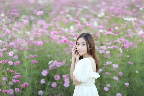 ピンクのコスモスの花の背景に白いドレスを持つ美しい若い女性 — ストック写真