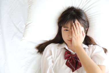 Japon okul üniformalı kız portresi uyur ve beyaz renkli yatak odasındaki kameraya bakar.
