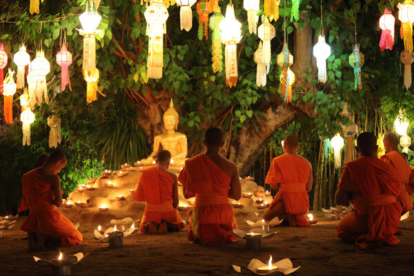 Thai monks meditate around buddha statue among many lanterns 