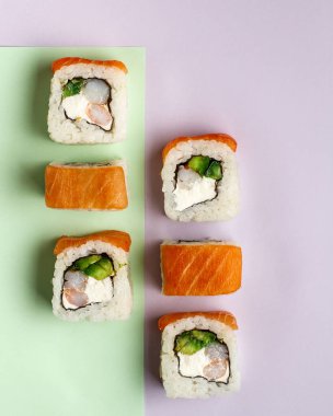 Pilav, somon, avokado ve krevotka ile Philadelphia ruloları. Renkli mor ve yeşil arka plan, üst manzara, yakın çekim.