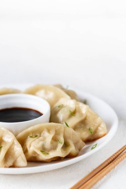 Japon Gedza 'sı yeşil soğanlı ve soya soslu sos soslu, beyaz tabakta, arka planda, yakın planda, çubuklarda.