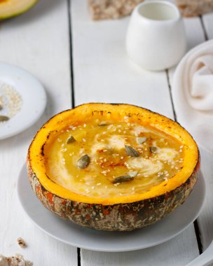 Kabak çorbası kabağı püresi bir tabakta, tohumlar ve kremayla süslenmiş beyaz tahta bir masada.