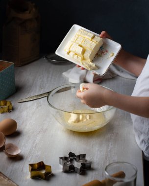 Çocuk kurabiye için hamur hazırlıyor, tereyağını hamurla şeffaf bir kaba koyuyor. Gri tablo.
