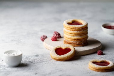 Ahşap bir tahtaya istiflenmiş kırmızı ahududu reçelli kurabiyeler, pudra şekeri serpiştirilmiş, gri arka plan, serbest alan