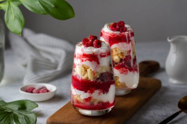 Trifles in layers with raspberries and whipped cream in glass glasses on a wooden board on the table. clipart