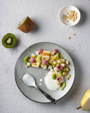 Ahududulu meyve salatası ve gri tabakta beyaz yoğurt ile tatlandırılmış kivi..