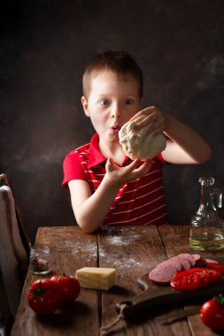 Çocuk hamuru ahşap bir masada hazırlıyor, kırsal bir mutfak, sürpriz bir duygu.