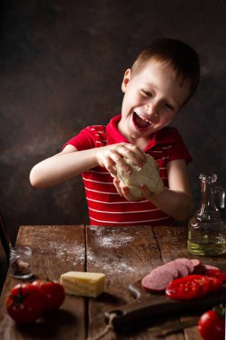 Bir çocuk hamurdan yemek pişirir, elinde bir top, neşeli duygular ve yüzünde mutluluk, bir gülümseme