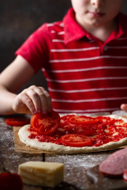 Bir çocuğun eli, yakın plan pizza için domates dilimlerini bir tabana serer..