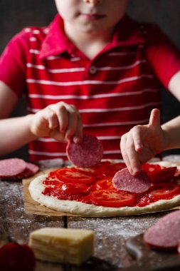 Bir çocuk pizza hazırlıyor, biberli daireler çiziyor, yakın plan.