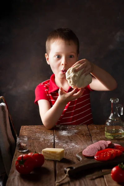 Çocuk hamuru ahşap bir masada hazırlıyor, kırsal bir mutfak, sürpriz bir duygu.