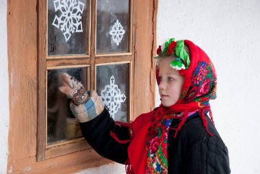 Noel kutlaması. Ulusal Ukrayna elbiseli küçük bir kız pencerenin önünde duruyor ve Noel 'den önce bir dilek tutuyor. KIEV, UKRAINE 