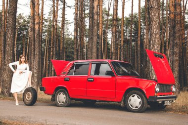 Chernigov, Ukrayna - 10 Kasım 2020: Arabanın yanında beyaz gelinlikli bir kız. Kız ve yedek lastik. Ormanda kırmızı retro araba