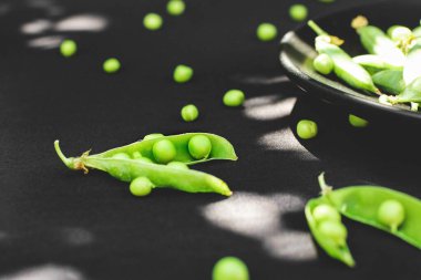 Siyah arkaplanda bezelyeler. Bir tabakta bezelye. Yaz meyveleri. Yeşil ve siyah