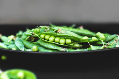 Siyah arkaplanda bezelyeler. Bir tabakta bezelye. Yaz meyveleri. Yeşil ve siyah