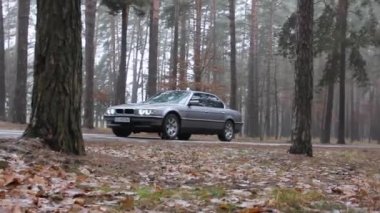 Chernigov, Ukrayna - 6 Ocak 2021: Eski BMW 7 Serisi (E38) ormanda yolda. Kasvetli hava. Farları açık araba.
